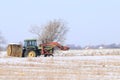A John Deere Farm Tractor hauling a hay bale on a road with snow