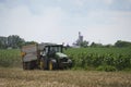 A John Deere tractor goes with a farm trailer on the farm. Background shows a corn field and a farm silo. Royalty Free Stock Photo