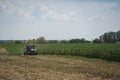 A John Deere tractor goes with a farm trailer on the farm. Corn field in the background. Royalty Free Stock Photo