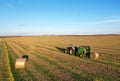 John Deere Tractor 6715R with John Deere V461R round baler making Hay Bales in an agricultural field. Farm Round Hay Bale Tractor Royalty Free Stock Photo