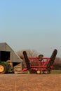 A John Deere tractor with a Sunflower oneway disc on the back with tree`s and blue sky with a barn.