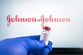 Johnson and johnson logo and covid-19 coronavaccine injection vial held with blue medical gloves.