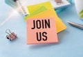 Join us sign on wooden cubes on pile of papers for notes at blue background Royalty Free Stock Photo