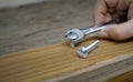 Joiner hand with a wrench screwing nut a furniture screw into a wooden plank, The effort wrong of tools as a fail concept