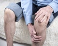 Joint disease, arthritis or arthrosis. Elderly man sitting on sofa and suffering from pain in knee