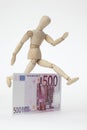 Jointed doll jumping over a 500-Euro-Banknote