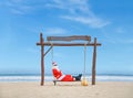 Jolly Santa Claus enjoying a day at the beach while seated in a swing.
