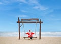 Jolly Santa Claus enjoying a day at the beach while seated in a swing.