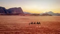 Jordan, Wadi Rum. Caravan of camels with drovers in the desert, rock mountains at sunset Royalty Free Stock Photo