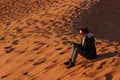 Woman sits on sand dune with smartphone at sunset