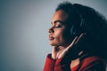 Joy of a music young African-American girl listening her favourite track in headphones wearing red jacket black top Royalty Free Stock Photo