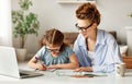 Joyful adult woman helping small girl to do homework in light spacious living room