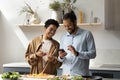 Joyful African American couple using cellphone, cooking in kitchen. Royalty Free Stock Photo