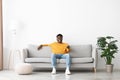 Joyful african american guy sitting on couch, turning on TV Royalty Free Stock Photo