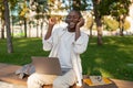 Joyful african american male student resting in campus with laptop, wearing headphones and enjoying music outdoors Royalty Free Stock Photo