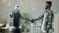 Joyful African American man shaking hand to manlike robot in workplace