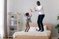 Joyful african american young man jumping on bed with son. Royalty Free Stock Photo