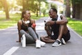 Joyful african couple resting after exercising outdoors, sitting on path in park Royalty Free Stock Photo