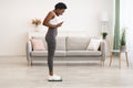 Joyful African Lady Weighing Herself After Diet On Weight-Scales Indoor