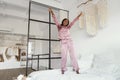Joyful African Woman Jumping On Bed Wearing Pajamas In Bedroom