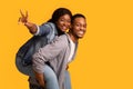 Joyful african woman piggybacking her boyfriend and showing peace gesture Royalty Free Stock Photo