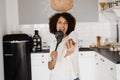 Joyful African young woman having fun with kitchen utensils. African american housewife in apron singing with spatulas Royalty Free Stock Photo