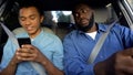 Joyful afro-american teen texting phone dad trying to read message while driving Royalty Free Stock Photo