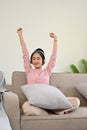 Joyful Asian girl listening music on headphones, raising hands and relaxing on her sofa Royalty Free Stock Photo