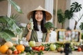 Joyful asian woman in traditional conical hat making smoothies using broccoli