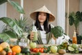 Joyful asian woman in traditional conical hat making smoothies using broccoli