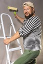 Joyful bearded craftsman with brush roller and ladder