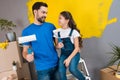 Joyful bearded father and little daughter plan to paint wall with rollers in yellow.