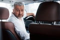 Joyful bearded man in white shirt looks into the camera while sitting in the modern car