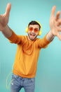 Joyful bearded young man wearing yellow sunglasses listening to music and take sefie over cyan background. Royalty Free Stock Photo