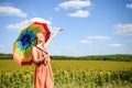 Joyful beautiful girl holding multicolored umbrella in sunflower field and blue cloud sky background Royalty Free Stock Photo