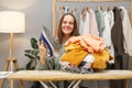 Joyful beautiful smiling Caucasian woman with brown hair ironing clothing while sitting in her wardrobe at home showing iron and Royalty Free Stock Photo
