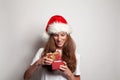 Joyful beautiful smiling woman in red Santa Christmas hat opening red gift on white background Royalty Free Stock Photo