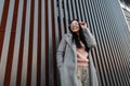 Joyful beautiful stylish young woman model in vintage long coat in pink sweatshirt with trendy glasses enjoys walk on the city on Royalty Free Stock Photo
