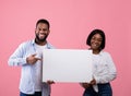 Joyful black couple holding and pointing at empty advertising board with copyspace on pink background, mockup for design Royalty Free Stock Photo