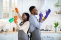 Joyful black couple using spray bottles as mics, singing during cleanup at kitchen Royalty Free Stock Photo