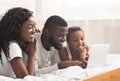 Joyful black family of three using laptop in bed together Royalty Free Stock Photo