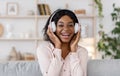 Joyful black girl with braces listening music in wireless headphones at home Royalty Free Stock Photo