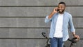 Joyful black guy standing with bike and talking on smartphone outdoors Royalty Free Stock Photo