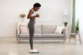 Joyful Black Lady Weighing Standing On Weight-Scales At Home