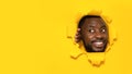 Joyful black man looking aside at copy space, standing in torn yellow paper hole, noticing pleasant unexpected offer Royalty Free Stock Photo