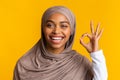 Joyful black muslim girl in hijab gesturing ok on yellow background