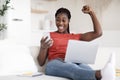 Joyful Black Woman Celebrating Success With Smartphone And Using Laptop At Home Royalty Free Stock Photo