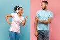 Joyful black woman dancing in wireless headphones, feeling happy, serious man making stop gesture, asking to calm down Royalty Free Stock Photo