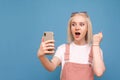 Joyful blond girl in a bright casual clothing holds a smartphone in her hands, looks at the smartphone screen and shouts.Surprised Royalty Free Stock Photo