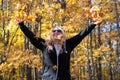 Joyful blond woman throws fall leaves in the air in a forest